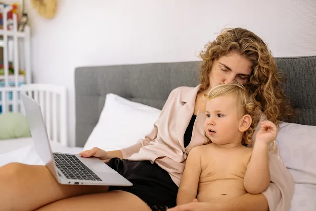 A mother and child relaxing together in bed, using a laptop. Family bonding indoors. Parenting creator checks: ICO code, food ads, ad labels, child licences and Companies House