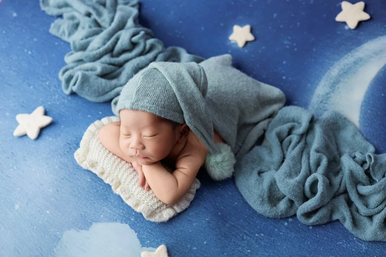newborn, creative photography, sleeping baby, blue color, moon and stars, baby studio, peaceful, baby hat, swaddle wrap, moonlight, newborn in studio, soft fabric, baby photography, fabric with stars, night sky, newborn with hat, snug baby, baby portrait, dreamy, newborn pose