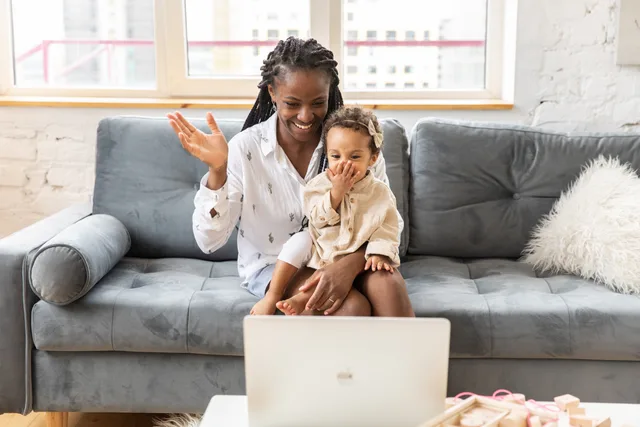 A joyful mother and daughter wave during a video call from their cozy living room couch. Parenting creator payment models compared for one family guide job