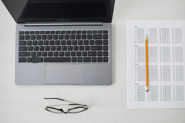 Flat lay of a laptop, exam sheet, and pencil on a white desk, perfect for education and technology themes. Reviewing products, platforms and agencies for parenting creators with family-safe test plans
